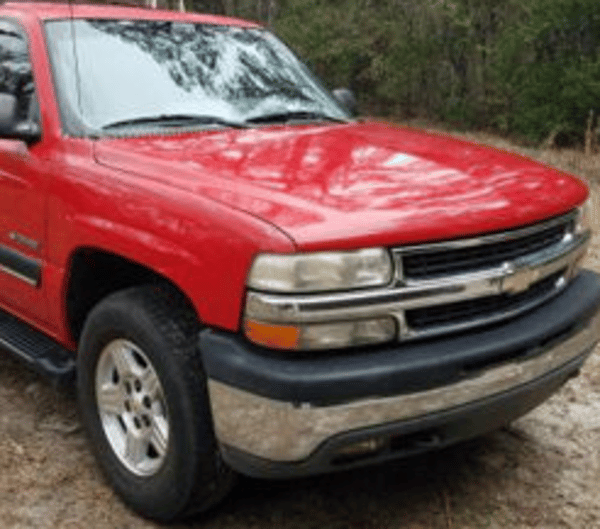 Red pickup truck parked on a gravel road beside trees