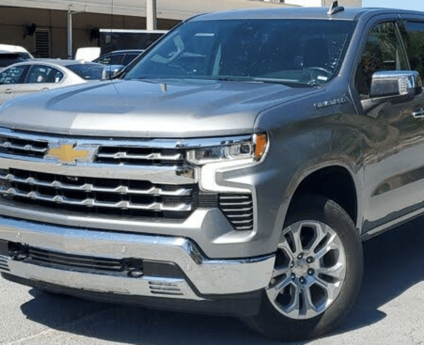 Silver Chevrolet SUV parked outdoors in a lot, front-left view, with chrome grille and gold emblem