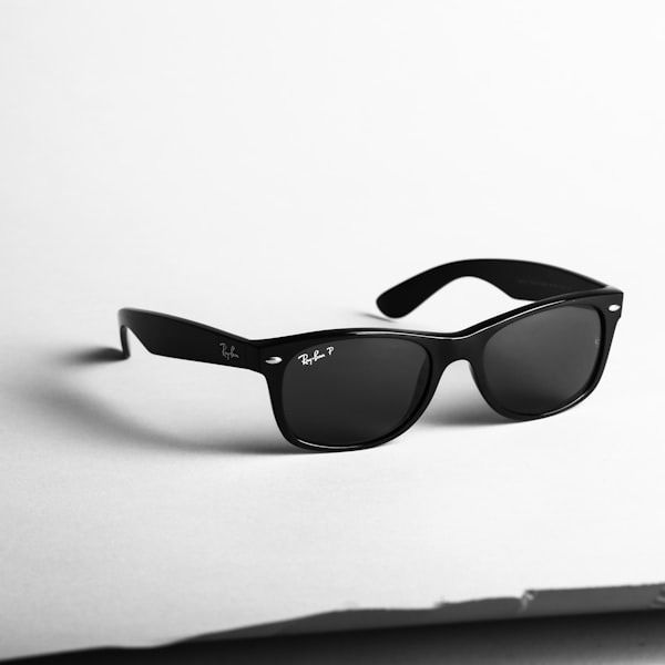 Black sunglasses with folded arms on a white surface, casting a shadow.