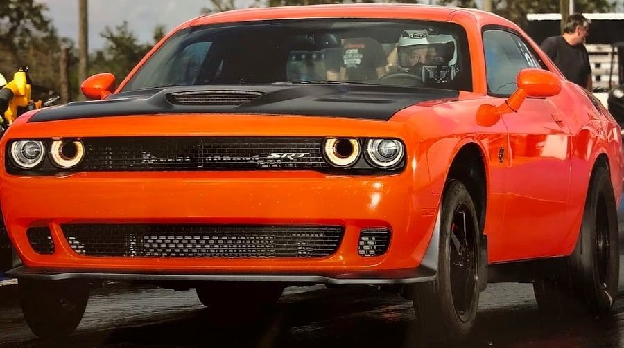 Bright orange Dodge Challenger sports car on a wet street, front view with headlights on
