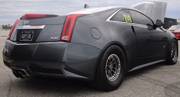 Black Cadillac CTS-V coupe parked on a lot, rear three-quarter view with aftermarket wheels and a large rear spoiler