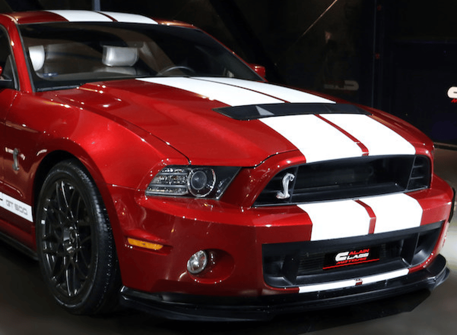 Red sports car with white racing stripes, front view in a dark garage