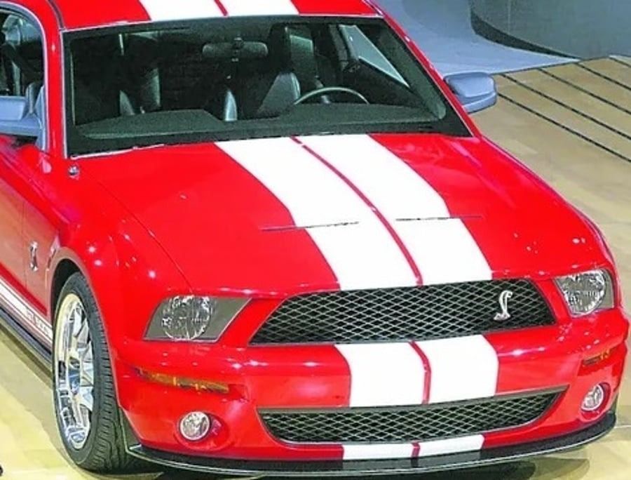 Red sports car with white racing stripes displayed indoors