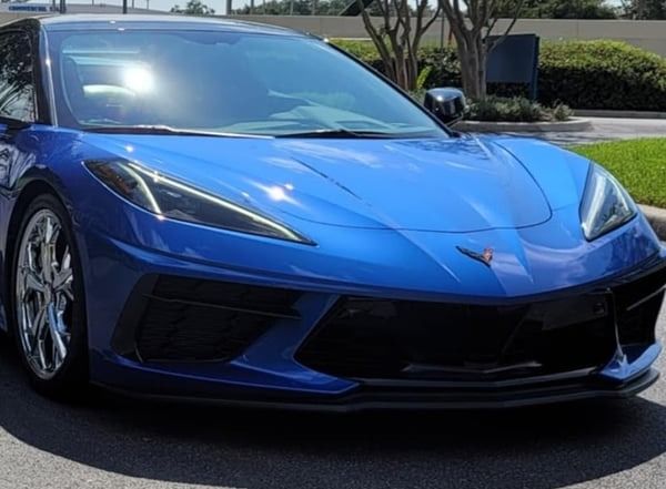 Blue sports car parked outdoors in sunlight, front view.