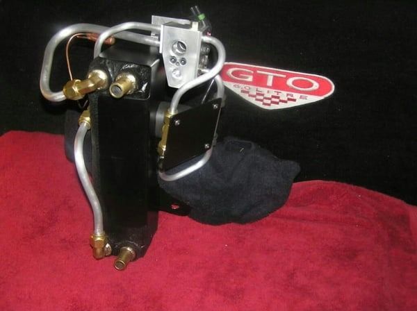 Black mechanical device with copper tubes and brass fittings on a red cloth, beside a GTO logo.