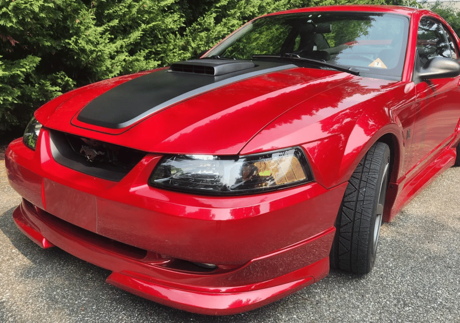 Red sports car with black hood stripe parked on a road by trees