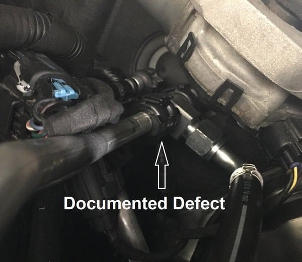 Close-up of engine hoses with arrow marking a documented defect.
