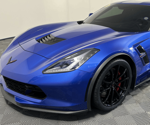 Blue sports car front view parked indoors with black wheels and hood vents