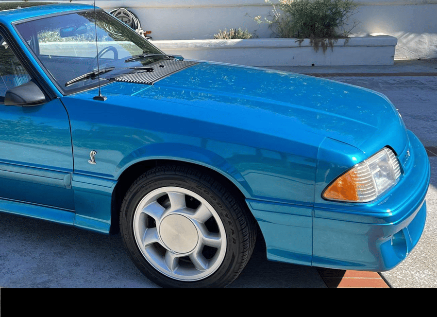 Blue sports car parked outdoors in sunlight, front side view