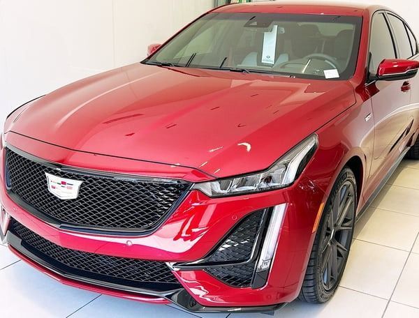 Red Cadillac SUV in a showroom, front-left view, on a white tiled floor.