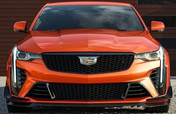 Front view of an orange Cadillac sports sedan on a dark road, showing its grille and headlights