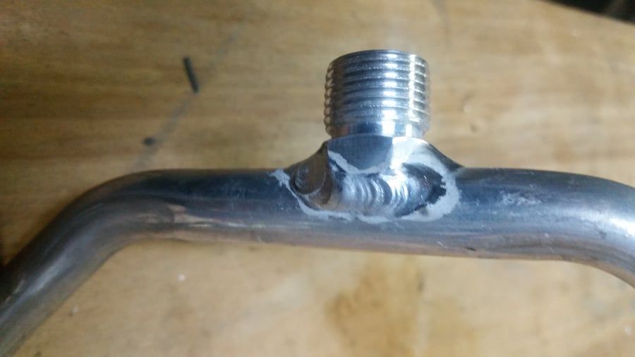 Close-up of a bent metal pipe with a threaded fitting welded to the center.