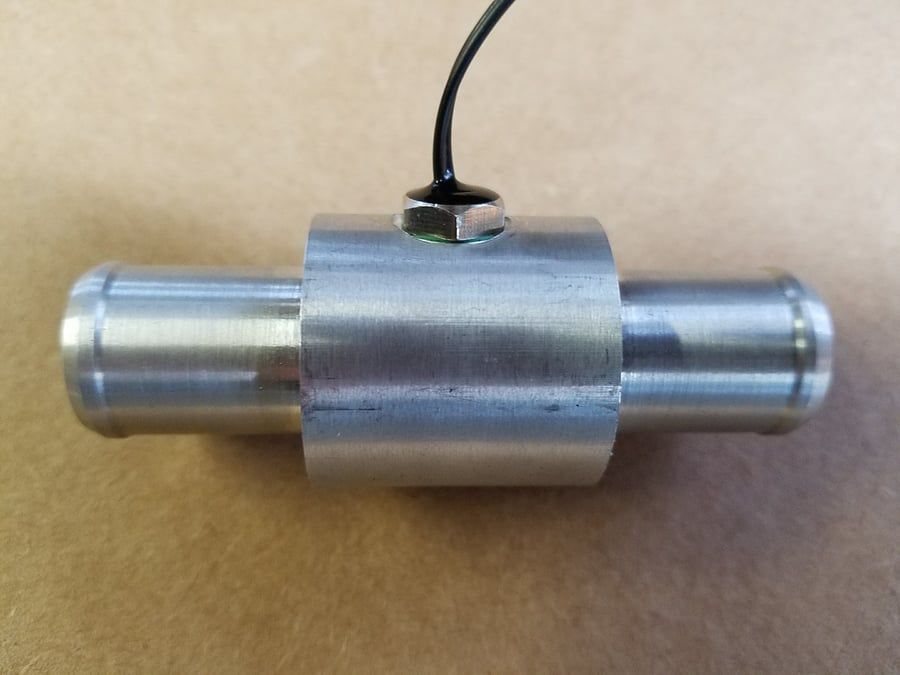 Small silver cylindrical metal sensor with a black wire attached, shown against a beige background