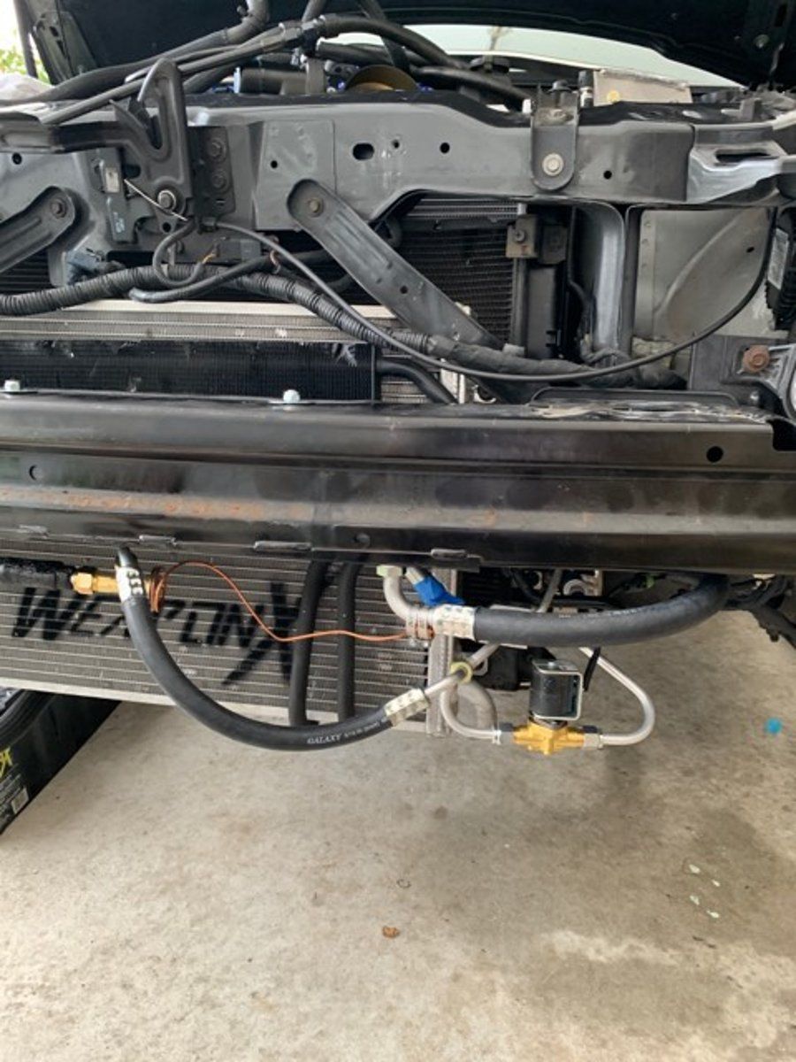 Front of a dismantled car in a garage, showing exposed frame and a detached fan assembly.