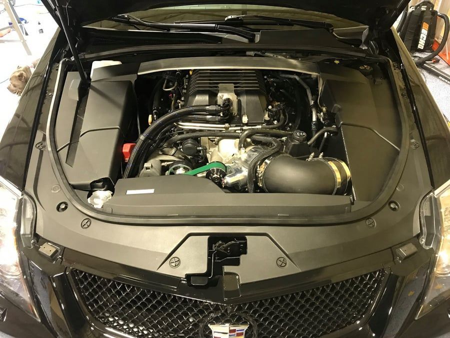 Open car hood revealing a black engine bay and front grille in a workshop.