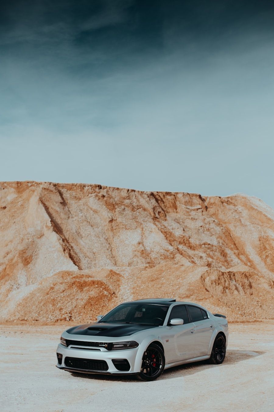 Silver sports coupe parked on a desert road with rocky cliffs in the background