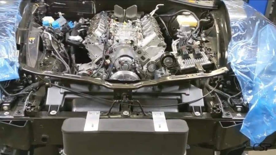 Car engine bay under repair, with exposed V8 engine and plastic covers around the chassis.