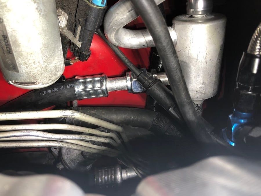 Close-up of car engine components with hoses, wires, and metal parts in red and silver.