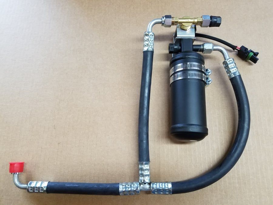 Black cylindrical filter assembly with hoses and metal fittings on a tan background