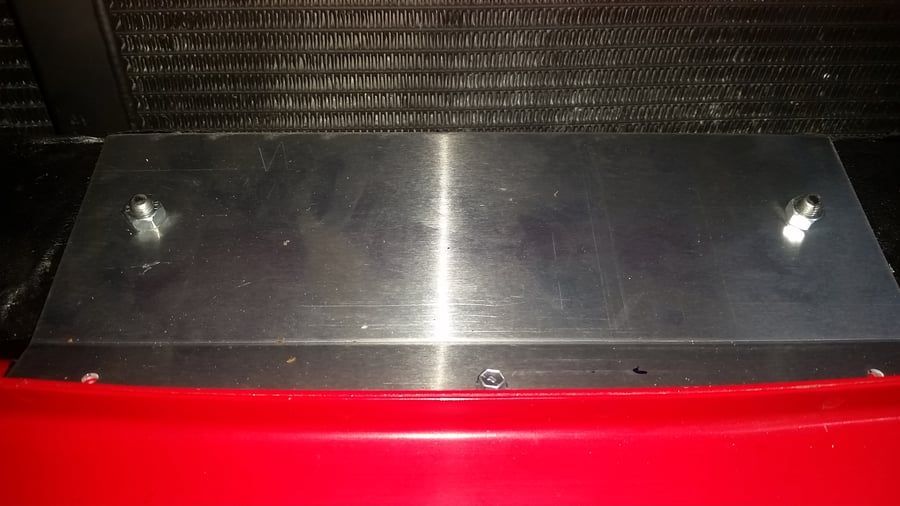 Red and black machine panel with a reflective metal top and two bolts at the back corners