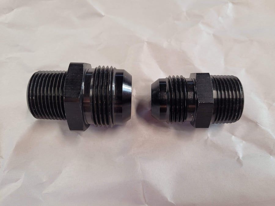 Two black threaded metal fittings with hex nuts, side by side on a white background