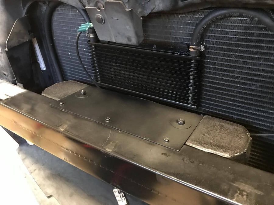 Close-up of a black vehicle radiator and metal bumper assembly inside an engine bay