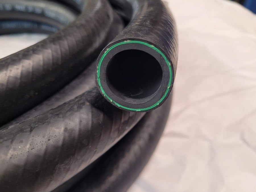 Coiled black rubber hose with green trim around the opening, shown close-up on a light surface