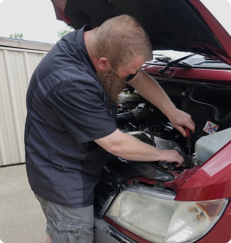Mechanic works on a red car's engine with a tool | Willamette Automotive Care