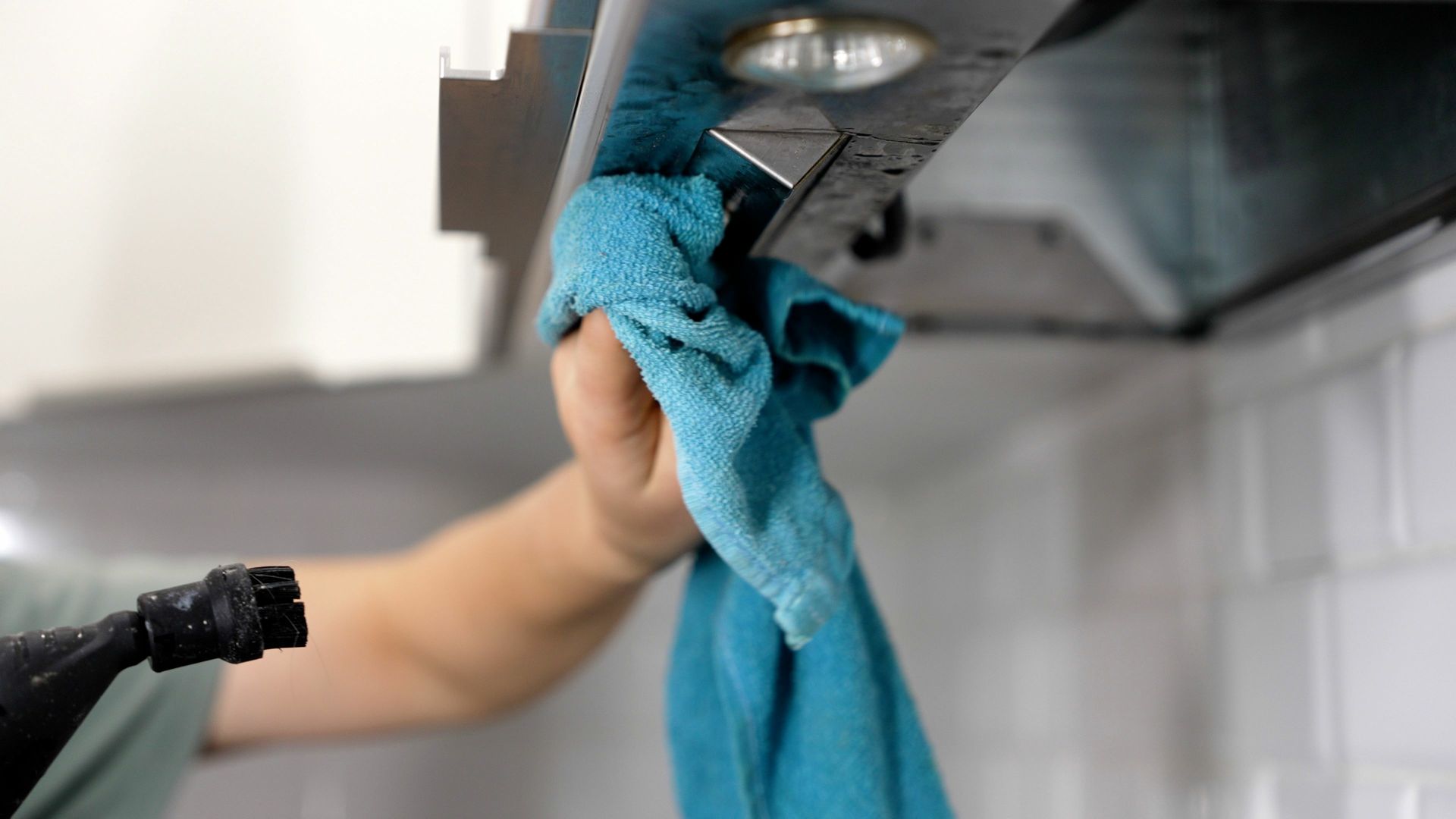 A person is cleaning a kitchen hood with a towel.