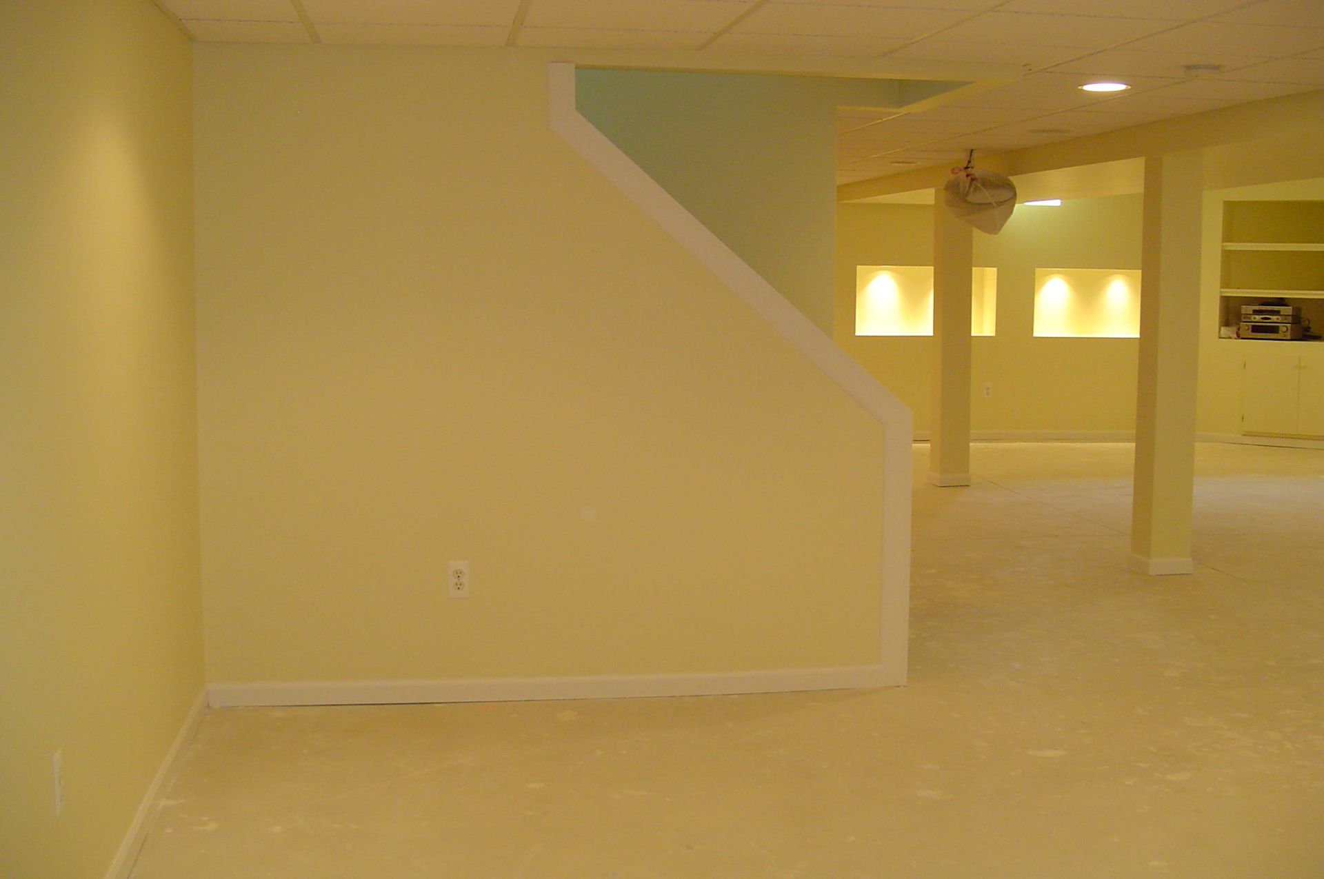 A finished basement with pale yellow walls and carpet, a staircase, and recessed lighting.