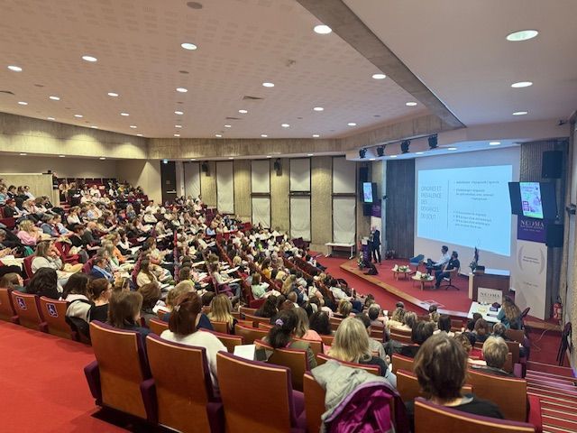 Un large public est assis dans un amphithéâtre à gradins, écoutant une présentation sur un écran placé à l'avant de la salle.