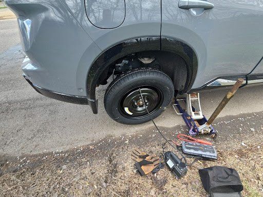 A car with a flat tire is sitting on the ground next to a jack.