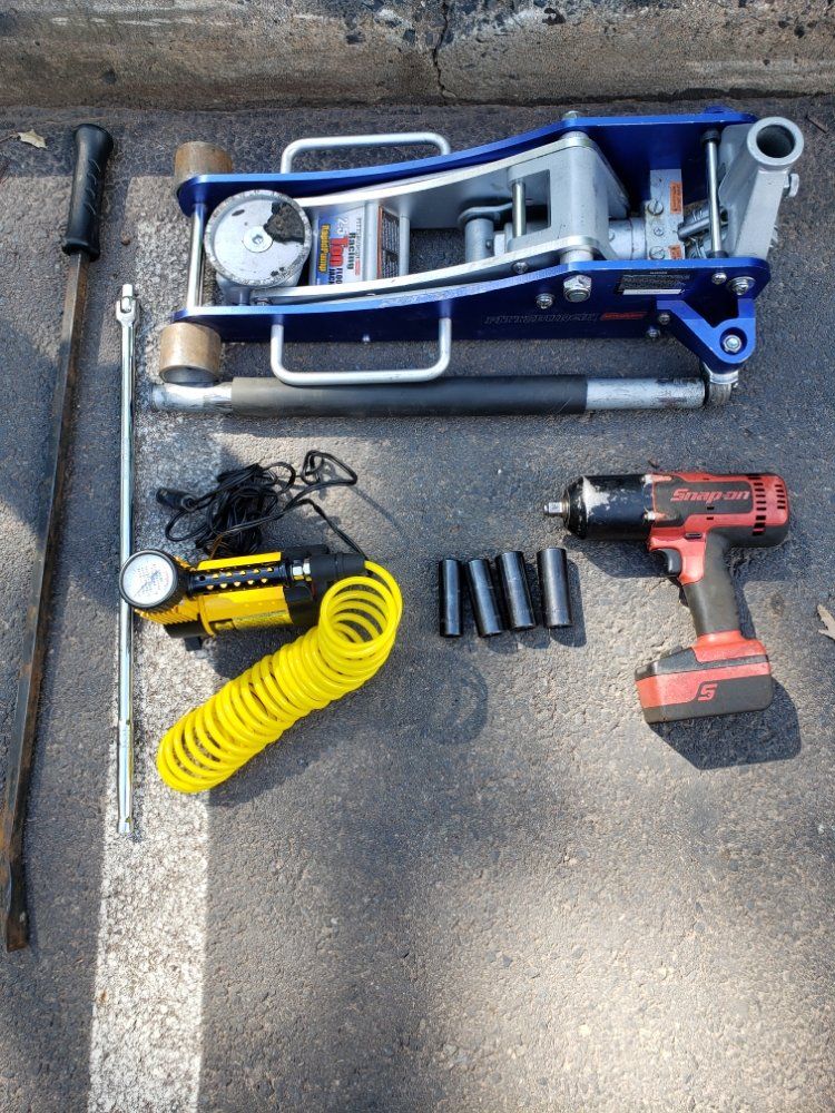 A jack , air pump , drill , and other tools are sitting on the ground.