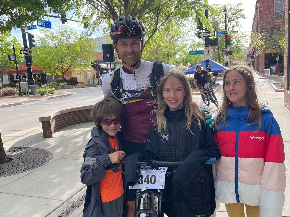 A man and three children are standing on a sidewalk next to a bicycle.