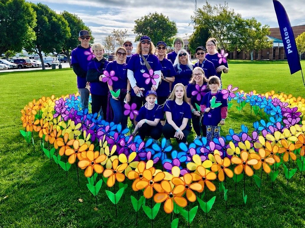 Group posing in a flower bed made of orange, purple, and yellow blooms in a park.