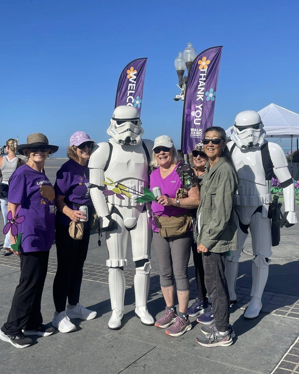 Five people posing with two Stormtroopers outdoors under a clear blue sky.
