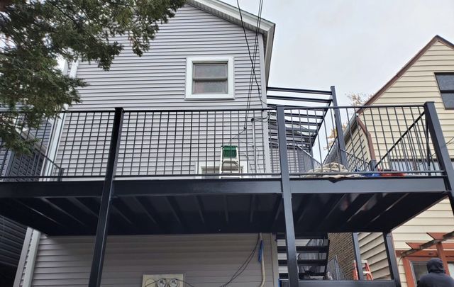 GALLERY. Black metal deck with railing, connected to a light gray house. Metal staircase visible. Cloudy sky.
