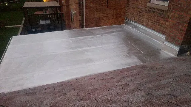 GALLERY. Flat roof with gray surface, adjacent to brick wall. Brown shingle roof in foreground.