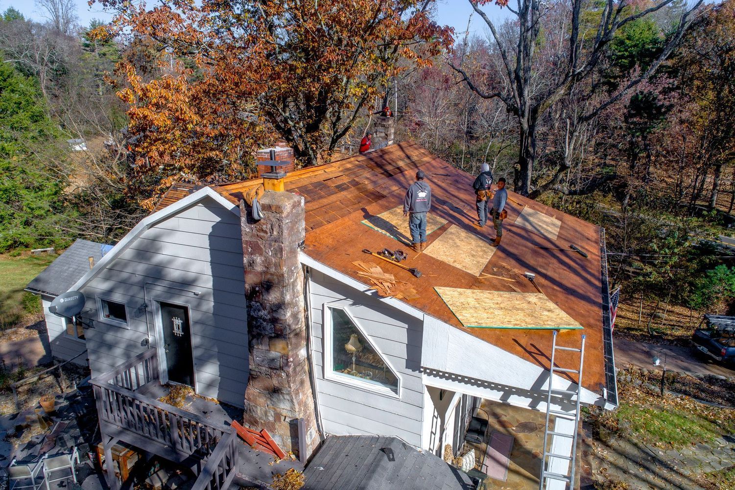 Roofing Contractor. Workers replace roofing shingles on a house with a chimney. Fall foliage is in the background.
