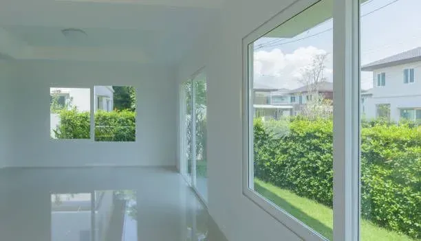Interior of a bright, white room with large windows overlooking a lush green yard and neighboring houses.