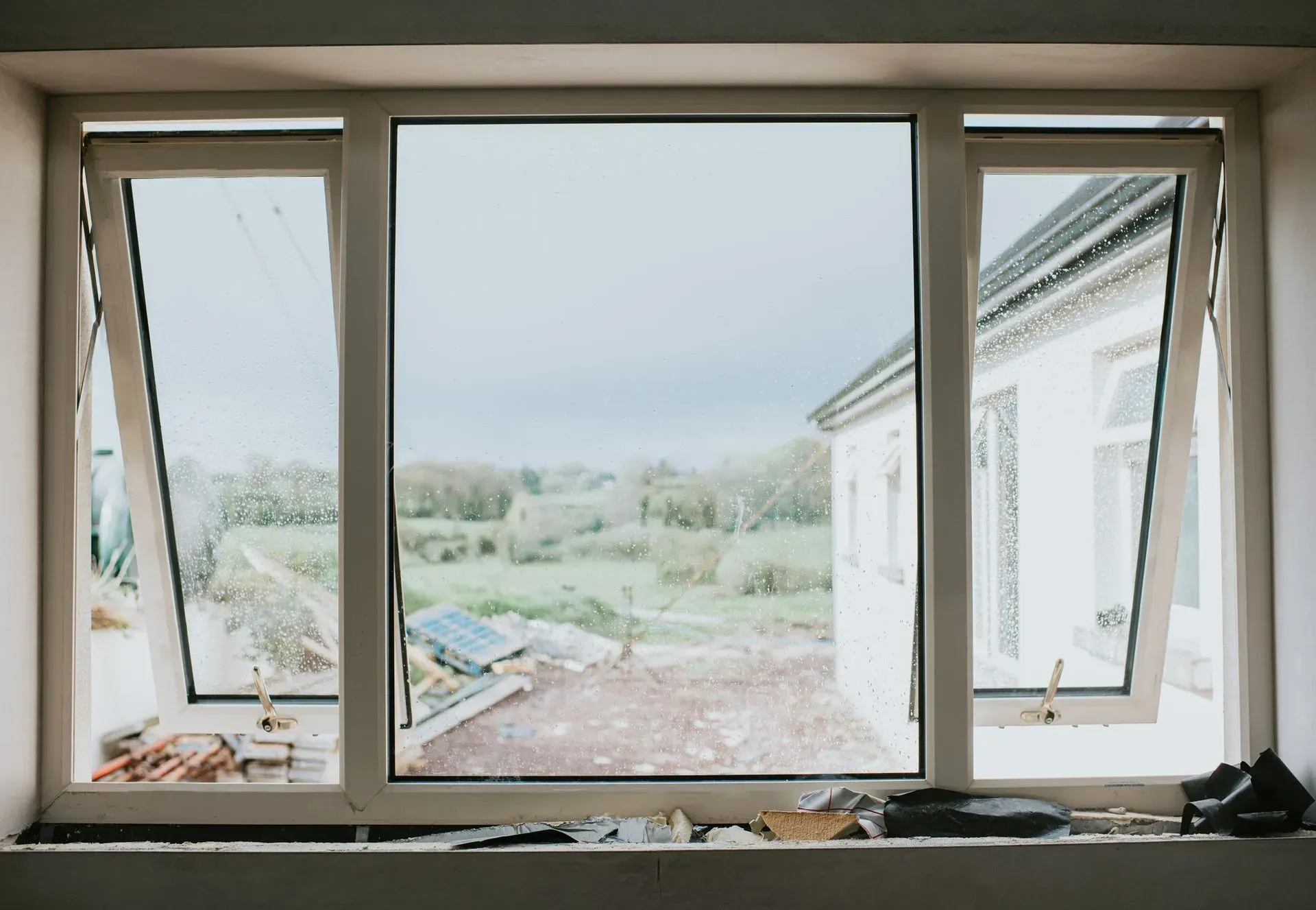 White-framed windows with angled panes overlooking a cloudy landscape and a white building.