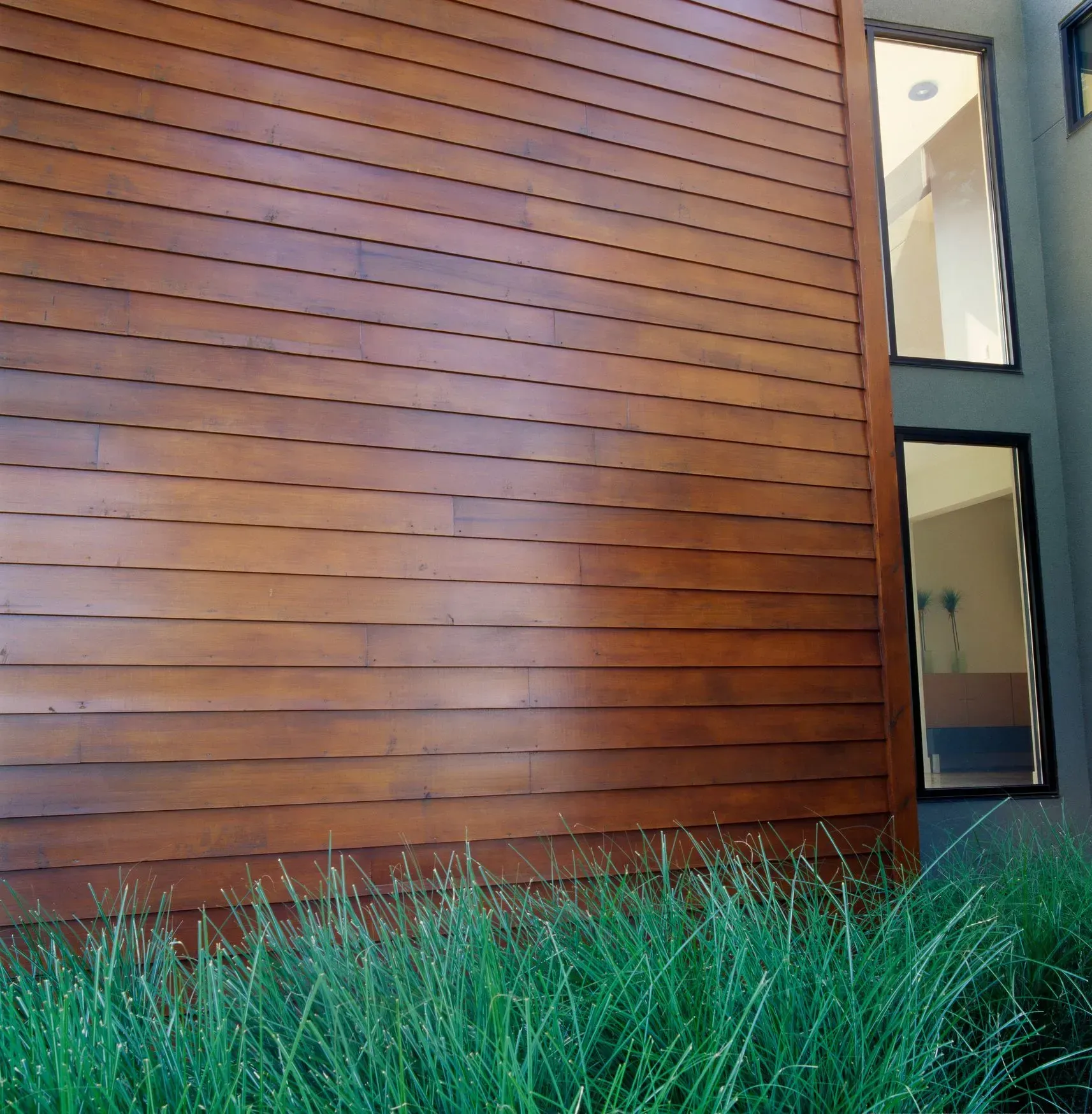 Exterior Services. Wooden siding on a building with two vertical windows, next to tall green grass.