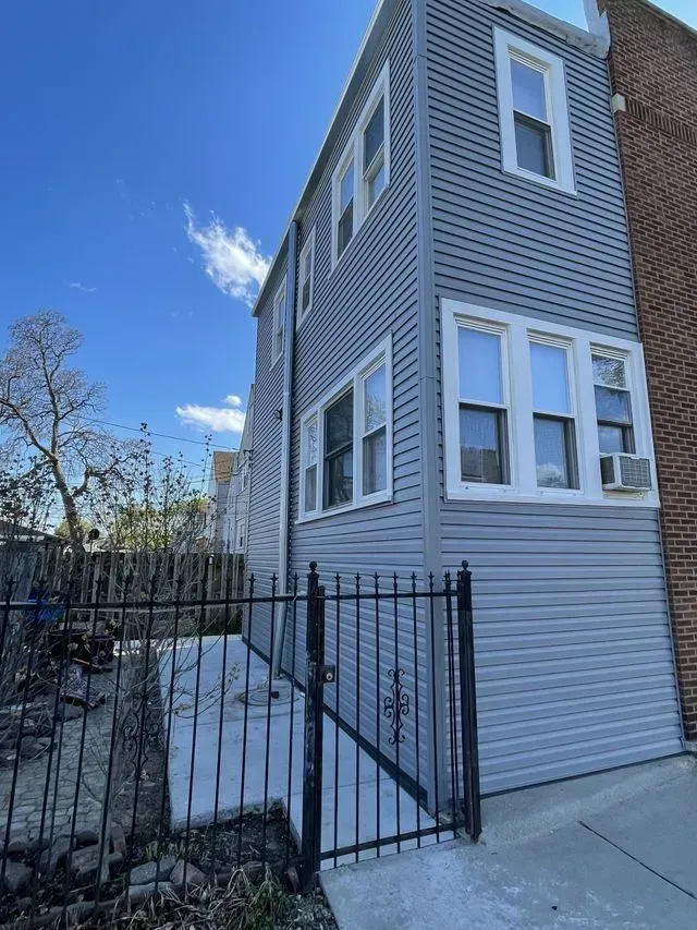 Gallery. Three-story house with gray siding, white window trim, and black wrought-iron gate against a blue sky.