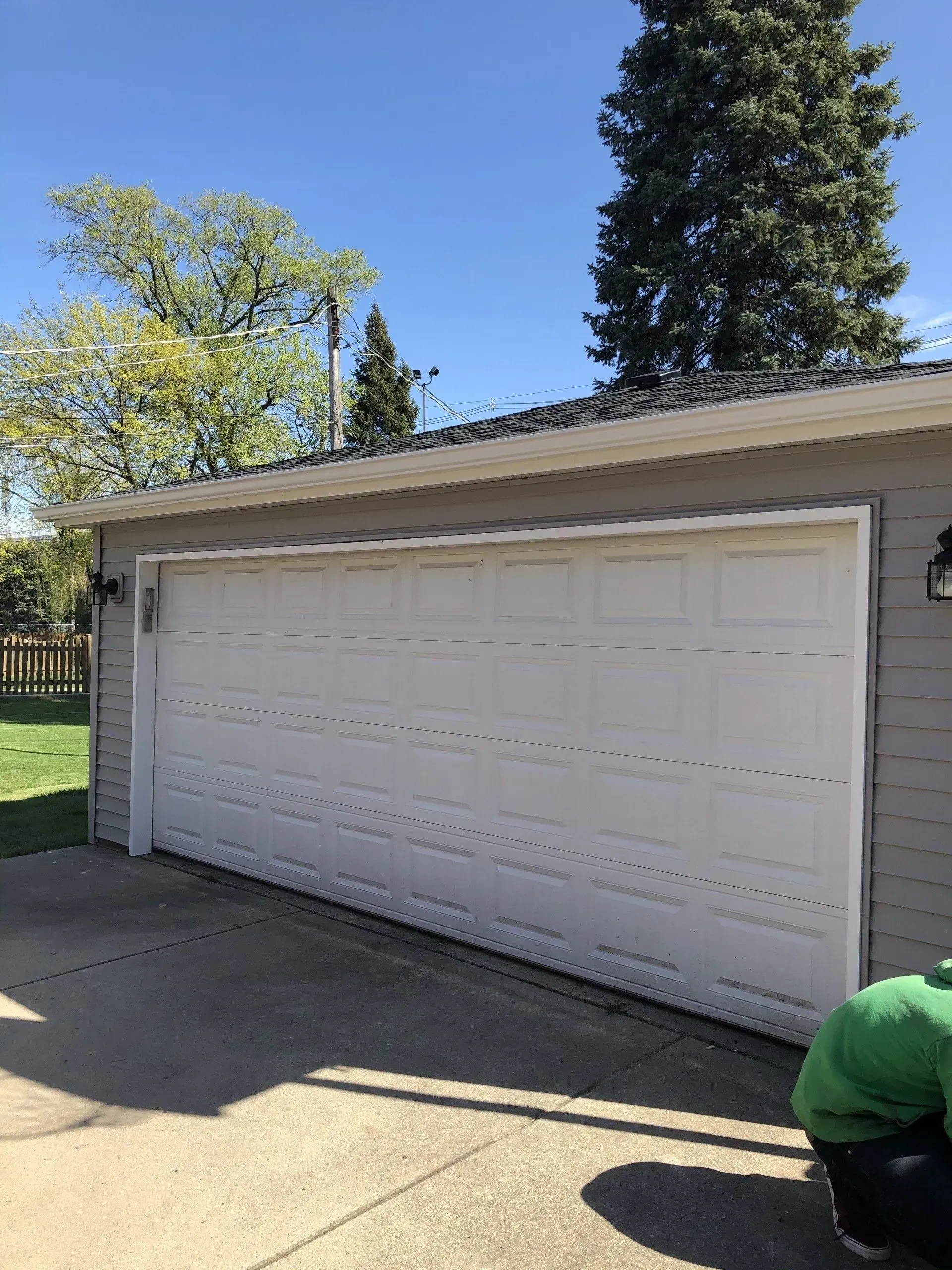 Gallery. White garage door, gray siding, concrete driveway, blue sky, and green trees.