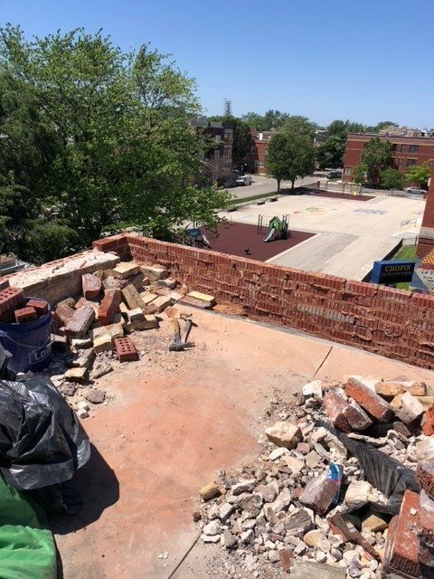 GARAGE. Roof demolition: red brick wall partially torn down, debris scattered across the flat surface, sunny outdoor setting.
