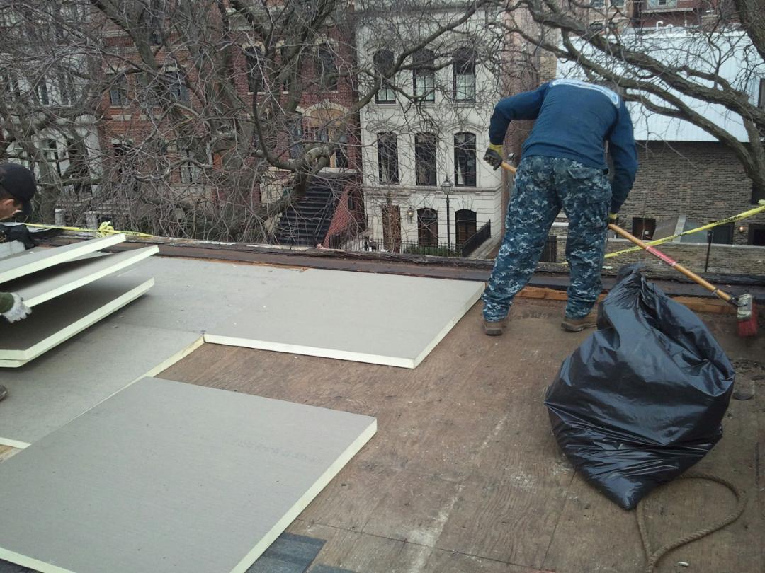 GARAGE. Construction worker installing insulation boards on a rooftop, with a black trash bag nearby.