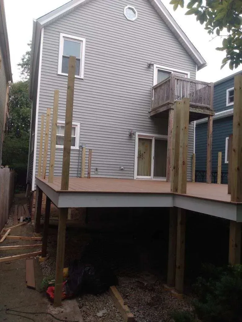 GALLERY. Newly constructed raised deck attached to a gray house, with unfinished wooden railings and supports.