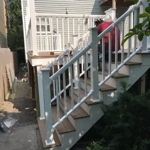 GARAGE. White railing staircase leads up to a deck. A person in red shirt is on the stairs.
