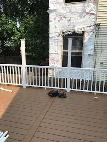 GARAGE. White deck railing and posts on a brown deck, near a house with exposed insulation.