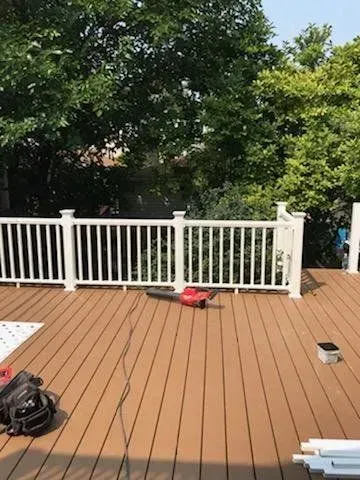 GARAGE. Wooden deck with white railing; red leaf blower in the center; trees in the background.